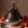 Traditional Uzbek cast iron pressure kazan pot with a locking lid, surrounded by fresh vegetables like tomatoes and bell peppers. Ideal for cooking pilaf, stews, and soups. Authentic cookware for Central Asian cuisine.